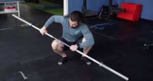 Dr. John pushing against one knee with a barbell do his squat warm up